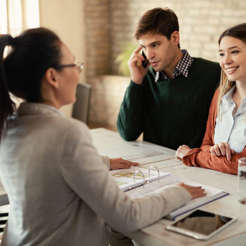 Happy woman talking with financial advisor while her husband is talking on the phone during a meeting in the office.